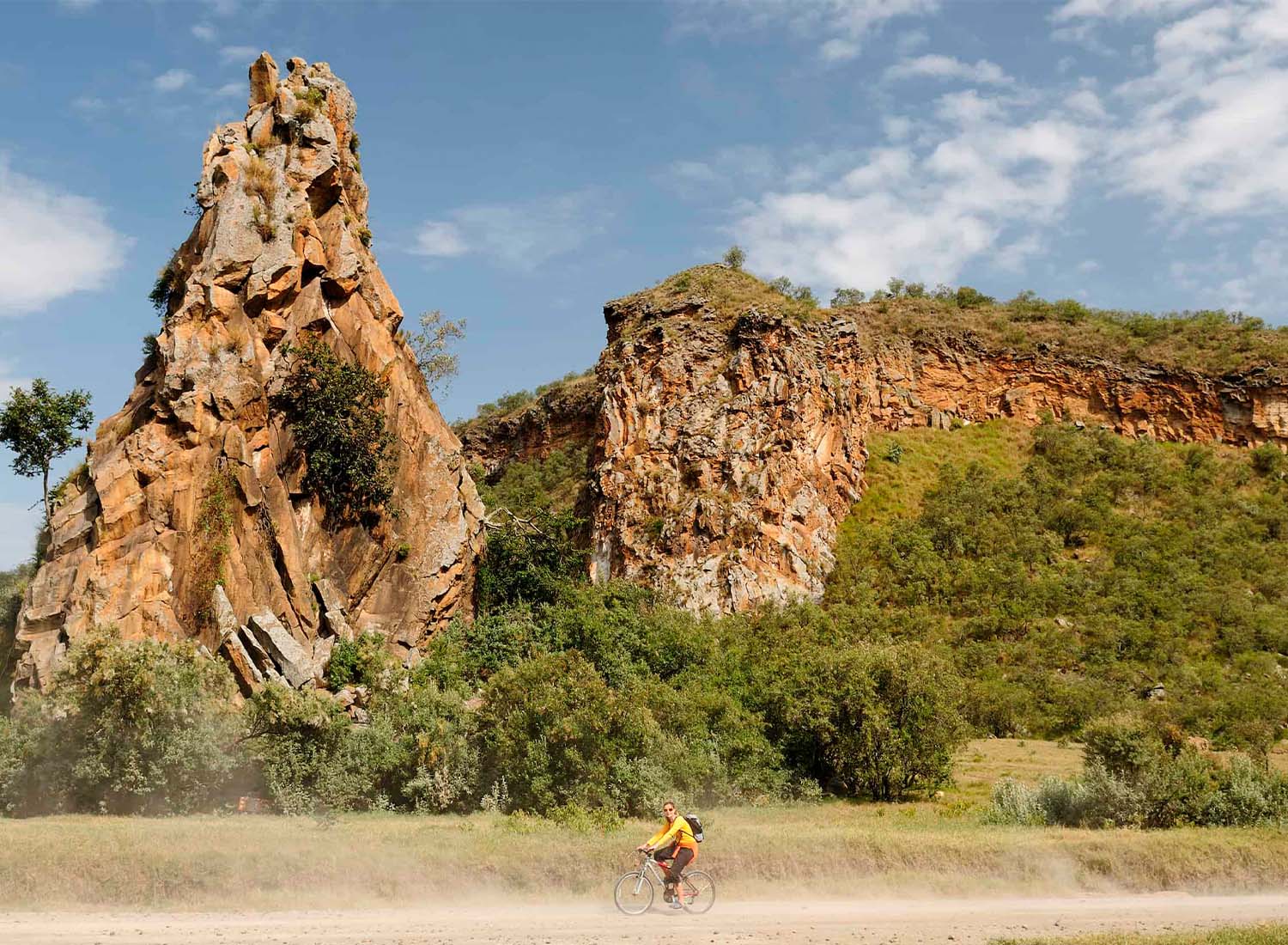 Tourist cycling through Hell's Gate National Park surrounded by zebras and dramatic cliffs