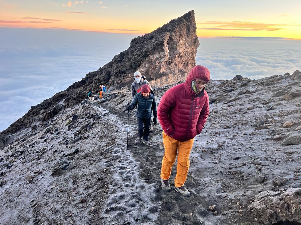 Climbers ascending Mount Meru's rocky ridge beneath clear skies during sunrise trek to summit.