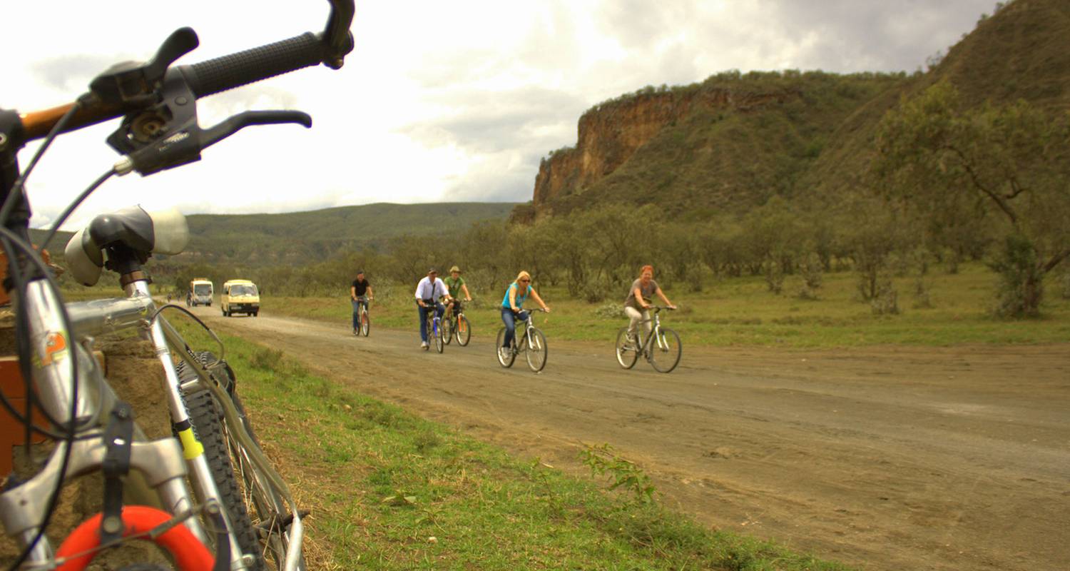 Cyclists riding through Hell's Gate National Park alongside zebras beneath towering cliffs in Kenya