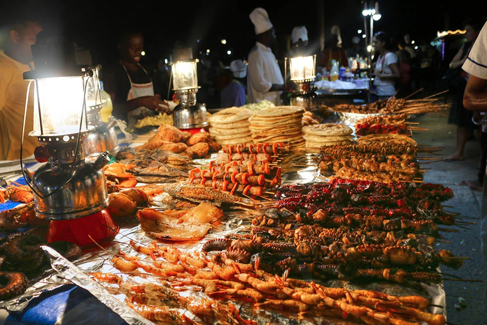 Fresh seafood vendors grilling delicious meals at Forodhani Gardens during vibrant Zanzibar evening market.
