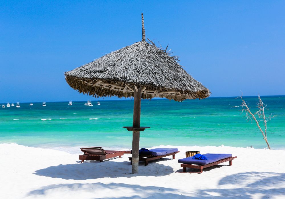 White sandy beach with turquoise ocean, palm trees, and traditional dhow sailing peacefully