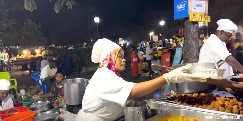 Visitors enjoying Zanzibar pizza beside ocean at Forodhani Gardens during sunset market.