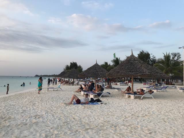 Tourists enjoying Kendwa Beach's white sand beside clear turquoise waters at sunset together.
