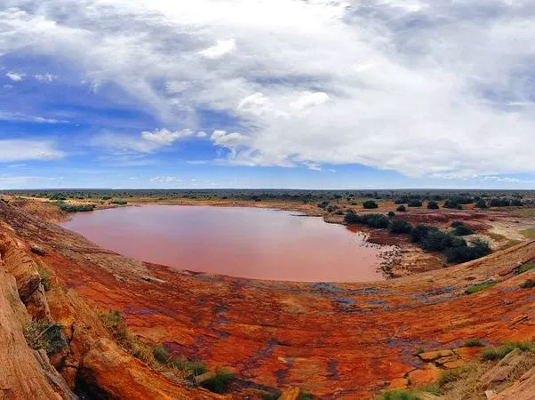 Mudanda Rock overlooking natural waterhole surrounded by rugged savannah beneath clear blue skies