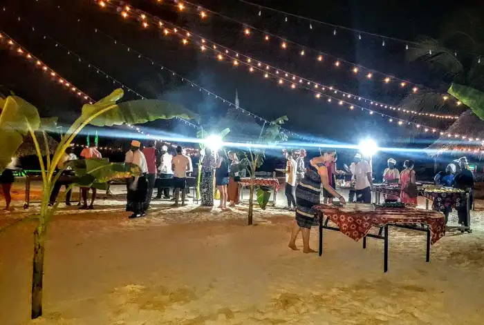 Friends dancing barefoot during Zanzibar full moon beach party beneath bright tropical night skies.