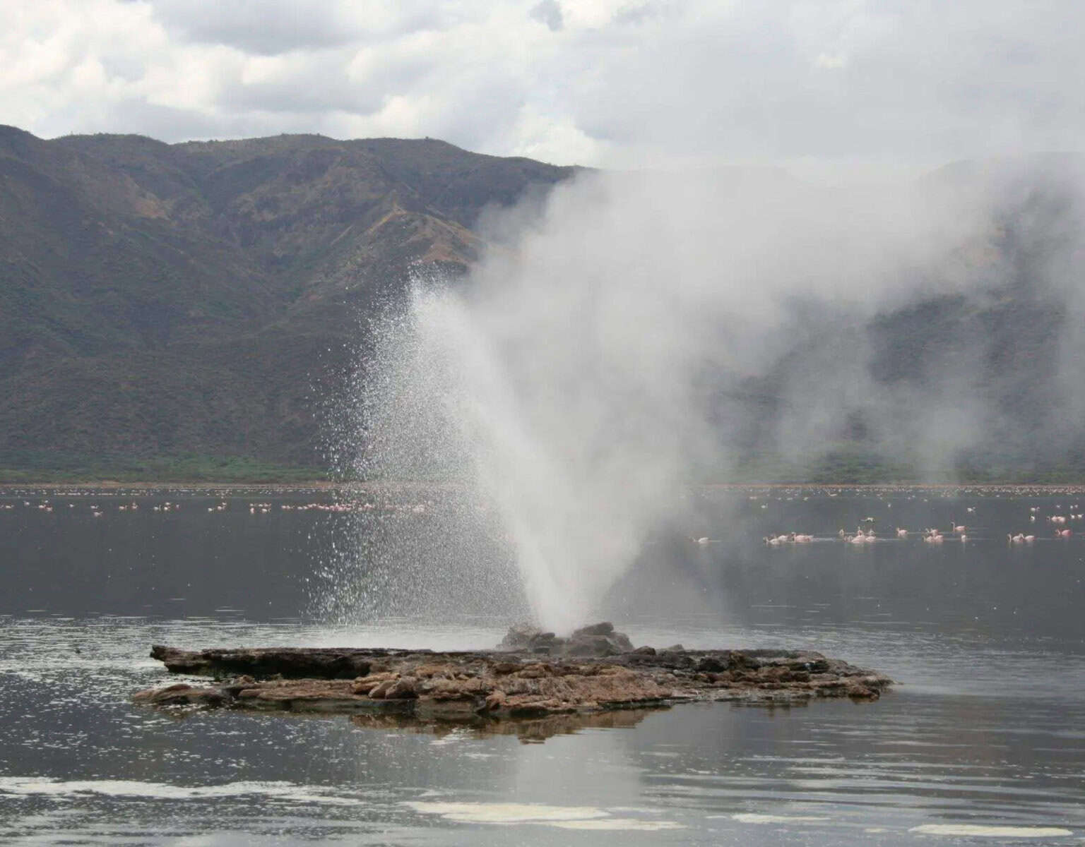 Steam rises from Lake Bogoria hot springs surrounded by rugged geothermal landscape and rocks.