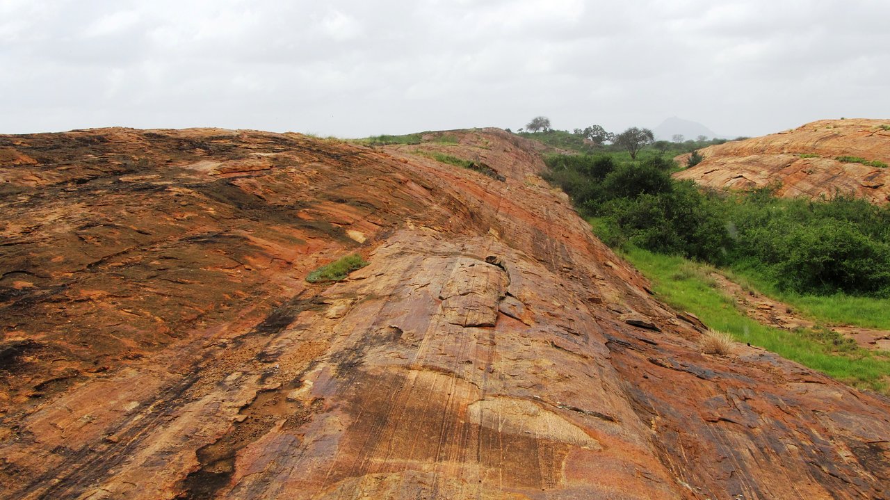 Mudanda Rock towering above natural waterhole surrounded by open grasslands under bright blue skies