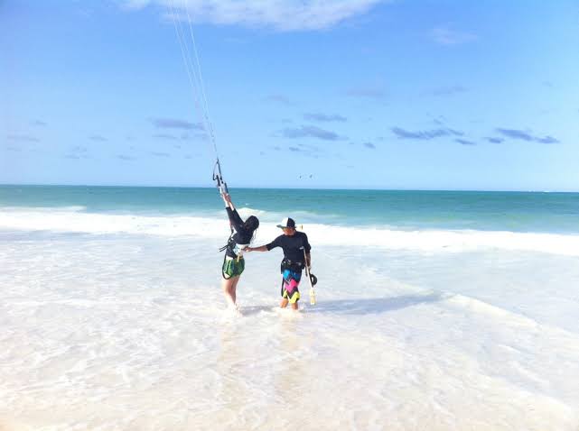 White sand beach with colorful kitesurfers riding turquoise Indian Ocean waves under clear tropical skies