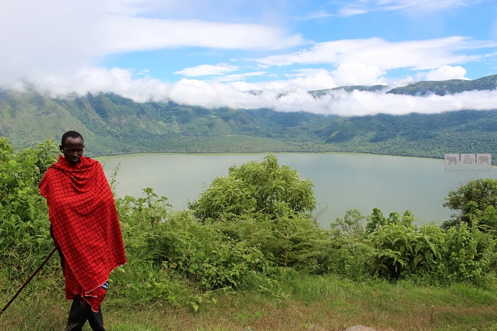 Volcanic crater lake surrounded by steep cliffs, forest, and hiking trail.