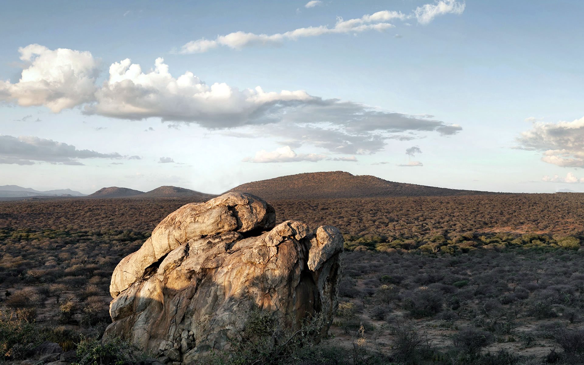 Rocky stone outcrops overlooking Laikipia Plateau with grazing zebras beneath clear blue skies.